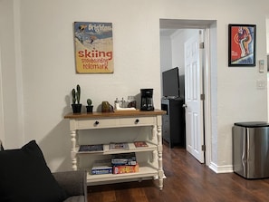 A living room with a wooden coffee table, a white entertainment unit with board games, a television, and a door leading to another room.