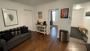 A living room with a grey sofa, a white coffee table, and a bookshelf. There is a door leading to another room. - The LIFTS: Downtown SLC/ Delta Center/ Pets OK! (Salt Lake City)