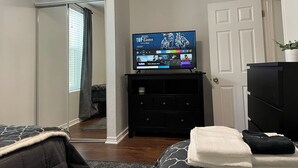 A bedroom with a bed, a TV on a dresser, a door, and a window with blinds. - The LIFTS: Downtown SLC/ Delta Center/ Pets OK! (Salt Lake City)