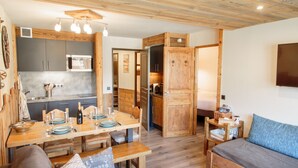 Una cocina moderna con armarios grises, una mesa de comedor de madera preparada para cuatro personas y una zona de estar acogedora con un sofá y un televisor.