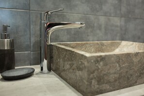 Une salle de bain moderne avec un lavabo rectangulaire en pierre, un robinet chromé et un distributeur de savon noir.