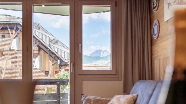 Una habitación acogedora con techo de madera, un sofá con cojines estampados y vista a un edificio de madera a través de una puerta de cristal.