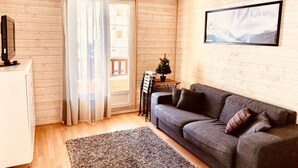 Ein gemütliches Wohnzimmer mit einem grauen Sofa, einem kleinen Tisch mit einer Pflanze und einer Holzwand.