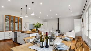 A modern kitchen with wooden cabinets, a dining table set for four, and a central island with a plant. - Botham's Beauty - Blenheim Holiday Home (Blenheim)