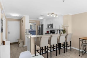 A modern kitchen with white cabinets, a central island with bar stools, a microwave, and a refrigerator. - Steps Away From The Ocean (North Myrtle Beach)