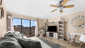 A living room with a sofa, TV, ceiling fan, and a dining area with chairs. - Steps Away From The Ocean (North Myrtle Beach)