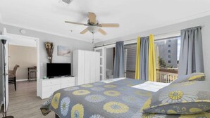 A bedroom with a bed, a ceiling fan, a television, a desk, and a view of a building through the window. - Steps Away From The Ocean (North Myrtle Beach)