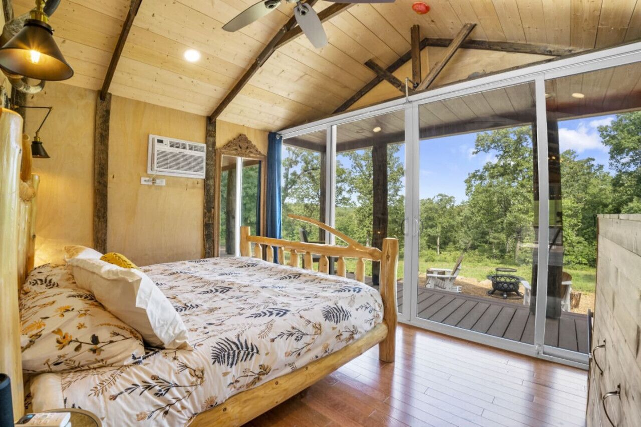 Un dormitorio con una cama de madera, un ventilador de techo y un amplio ventanal corredera que da a una terraza exterior.