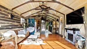 A log cabin interior with a wooden ceiling, a hanging chair, a fireplace, and a television mounted on the wall. - Tiny Houses of French Village Tranquil & Relaxing (French Village)