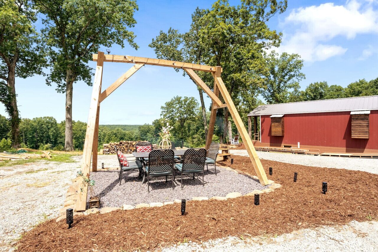 A wooden swing set, outdoor seating, and a red building in a landscaped area.