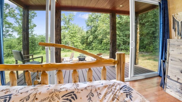 A wooden deck with a bed and a table, overlooking a forested area. - Tiny Houses of French Village Tranquil & Relaxing (French Village)