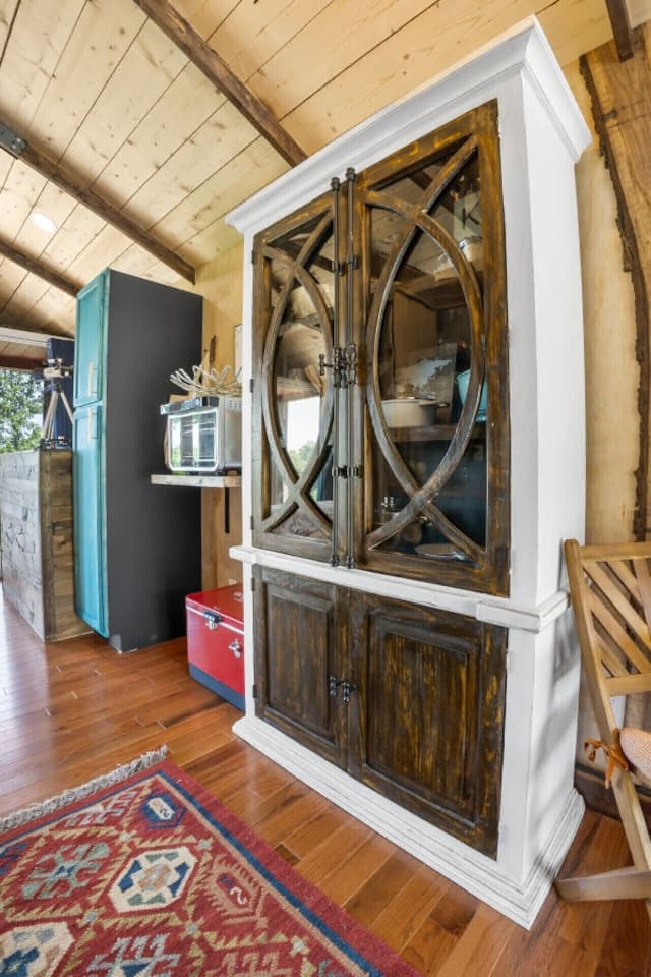 Un meuble en bois avec des portes en verre et une valise rouge posée sur un plancher en bois.