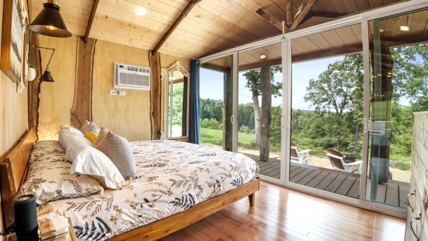 Ein Schlafzimmer mit einem großen Bett, Holzboden und Blick ins Freie.