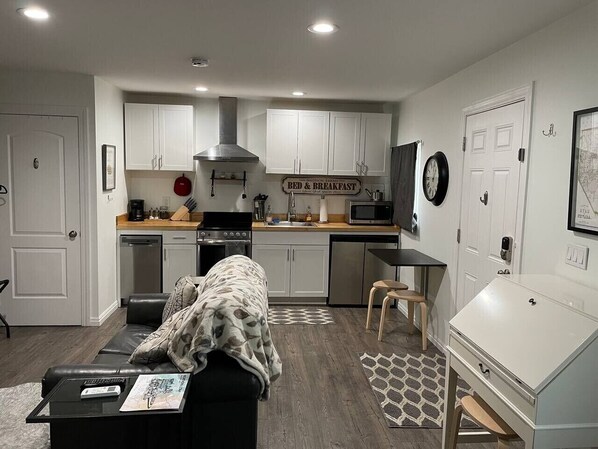 Cocina compacta con armarios blancos, microondas y estufa. Cuenta con un comedor con una silla y una mesa.