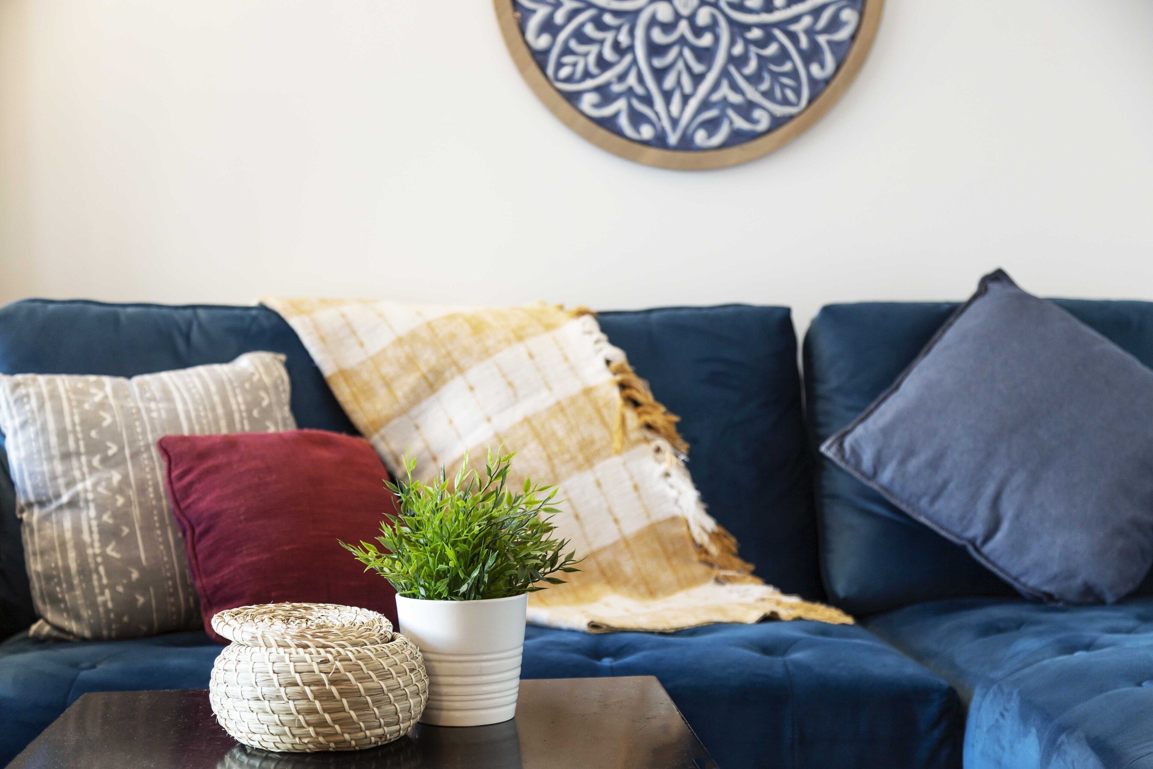 A blue sofa with patterned cushions, a woven basket, and a potted plant on a dark wooden table.