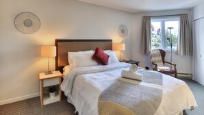 Une chambre d’hôtel avec un lit bien fait, deux lampes de chevet, une chaise et une vue sur l’extérieur par une fenêtre.