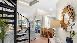 Ein modernes Interieur mit einer Wendeltreppe, einem Essbereich mit Korbmöbeln und einem dekorativen Spiegel an der Wand.