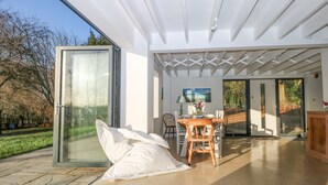 A modern interior with a glass door leading to a garden, a dining area with a table and chairs, and a wooden cabinet. - Meon Boscage (Southampton)