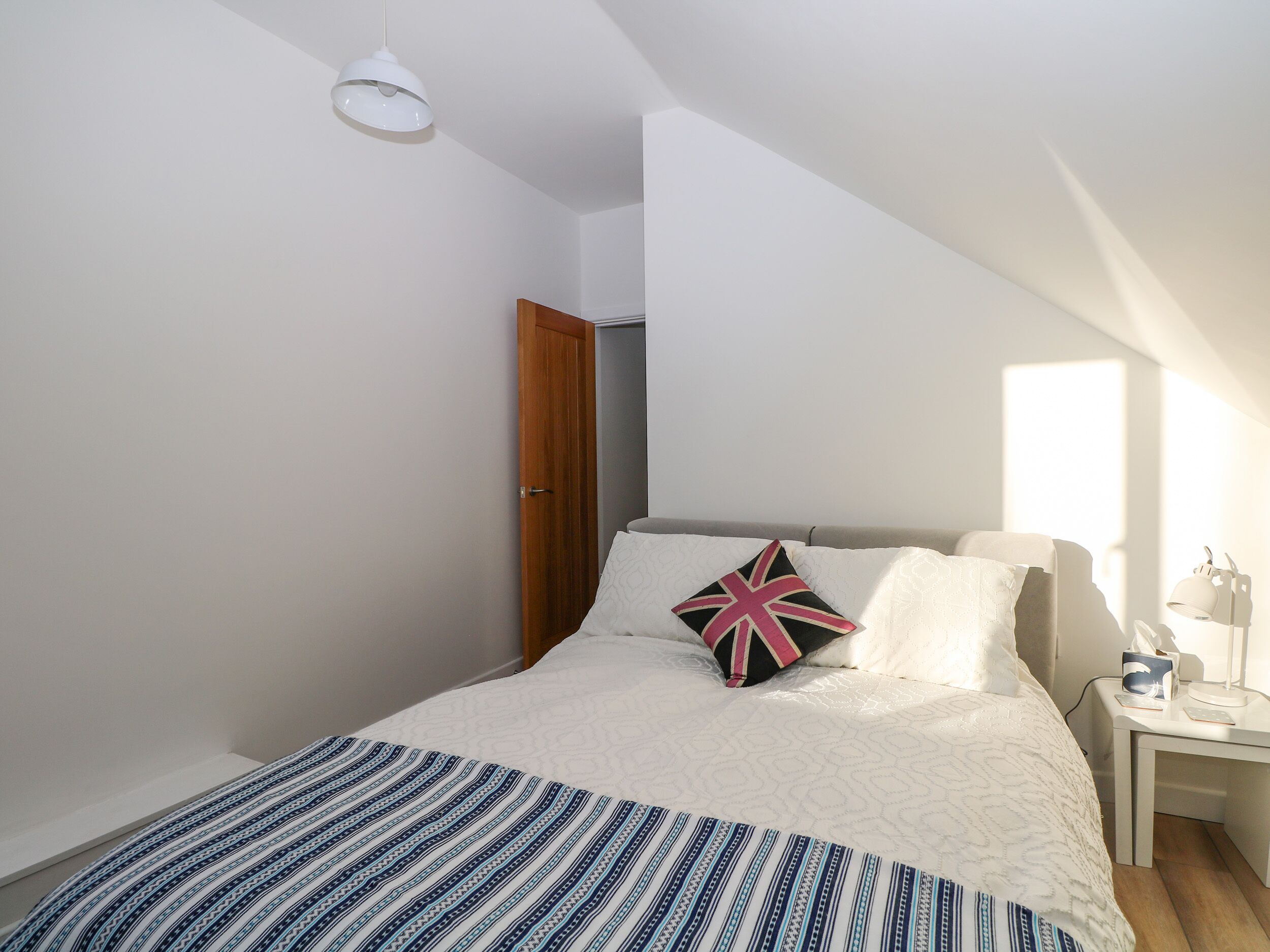 Une chambre moderne avec un grand lit, une table de chevet avec une lampe et une porte donnant sur une autre pièce.