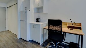 Une cuisine de taille réduite, avec des meubles blancs, un réfrigérateur et une machine à café.