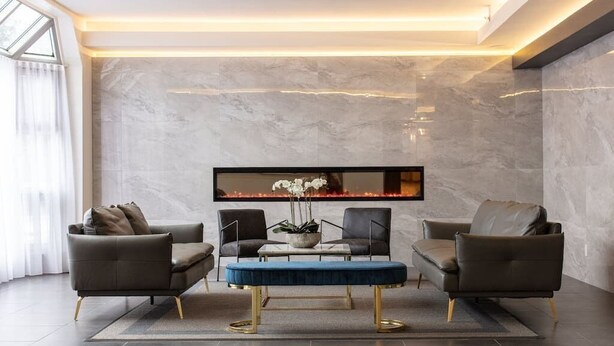 Un salon moderne avec un mur en marbre, un téléviseur à écran plat et deux canapés en cuir.