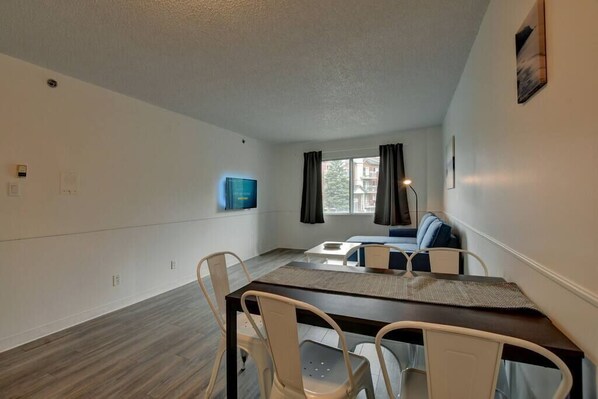 A modern, well-lit room with a dining table and chairs, a sofa, and a window with curtains.