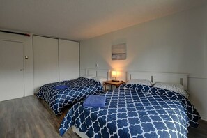 A bedroom with two beds, a nightstand with a lamp, and a door.
