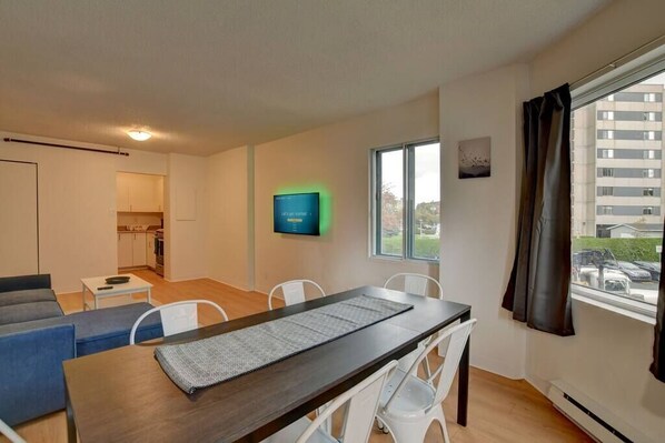 Un apartament modern amb zona de menjador, cuina i televisió penjada a la paret.