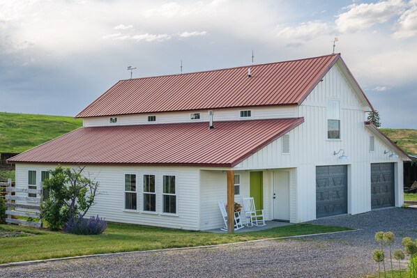 A white barn with a red roof, two garage doors, and a green door. - Custom, Countryside Barndominium for Multi-Family near Bozeman with Hot Tub (Manhattan)
