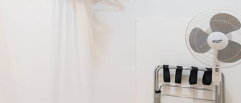 Una habitación con piso de madera, un tendedero, un ventilador y una cama con colchón blanco y ropa de cama estampada.