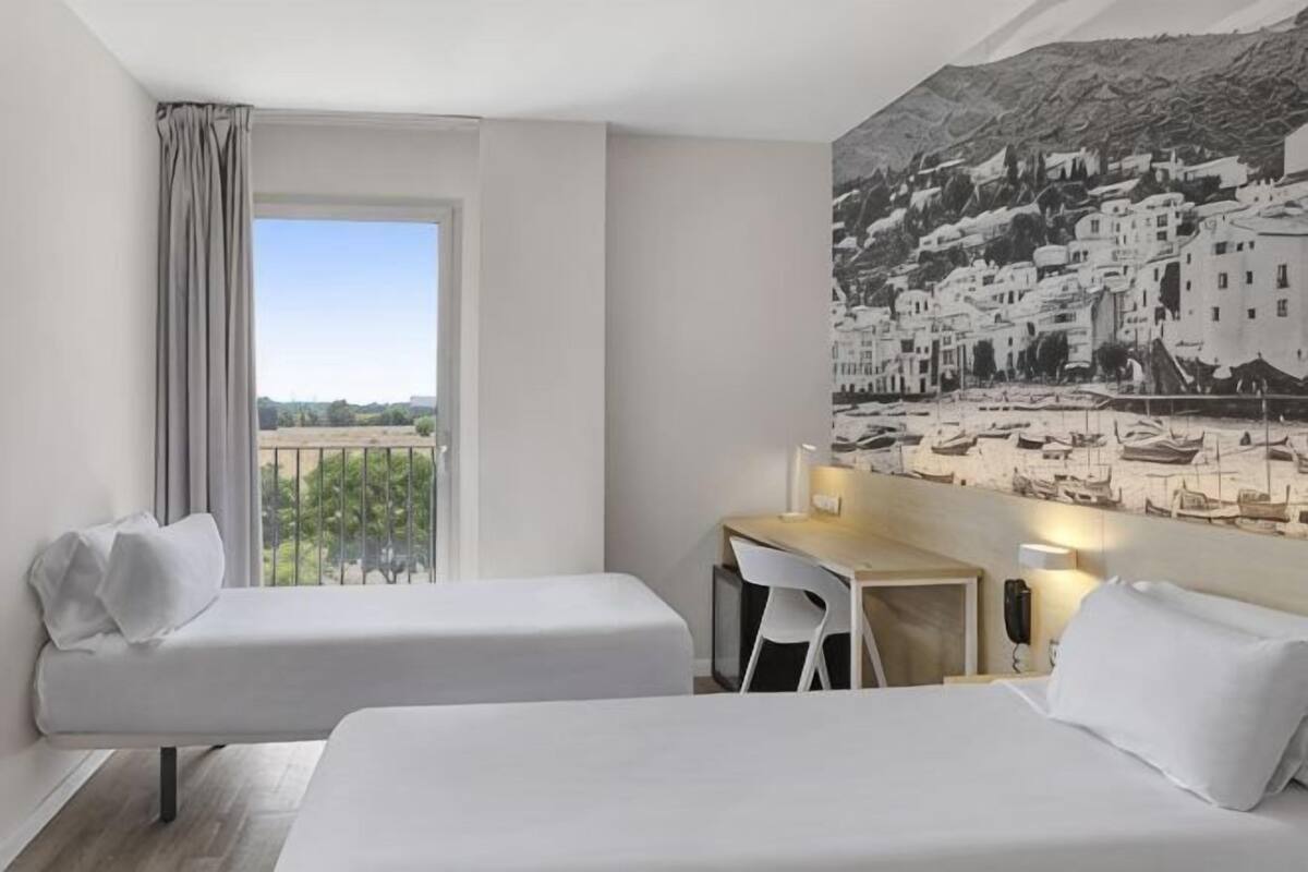 A hotel room with two beds, a desk, and a chair.