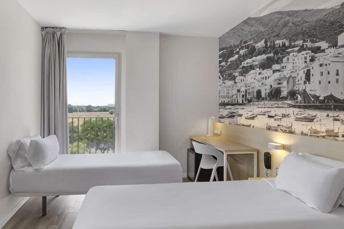 A hotel room with two beds, a desk, and a chair.
