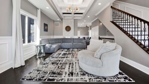 A spacious living area with a large sectional sofa, a round white armchair, a patterned rug, and a staircase with a black railing. - Lux Home in Chicago 7mins Downtown (Chicago)