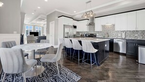 A modern kitchen with white cabinets, a central island, bar stools, and a dining table with chairs. - Lux Home in Chicago 7mins Downtown (Chicago)
