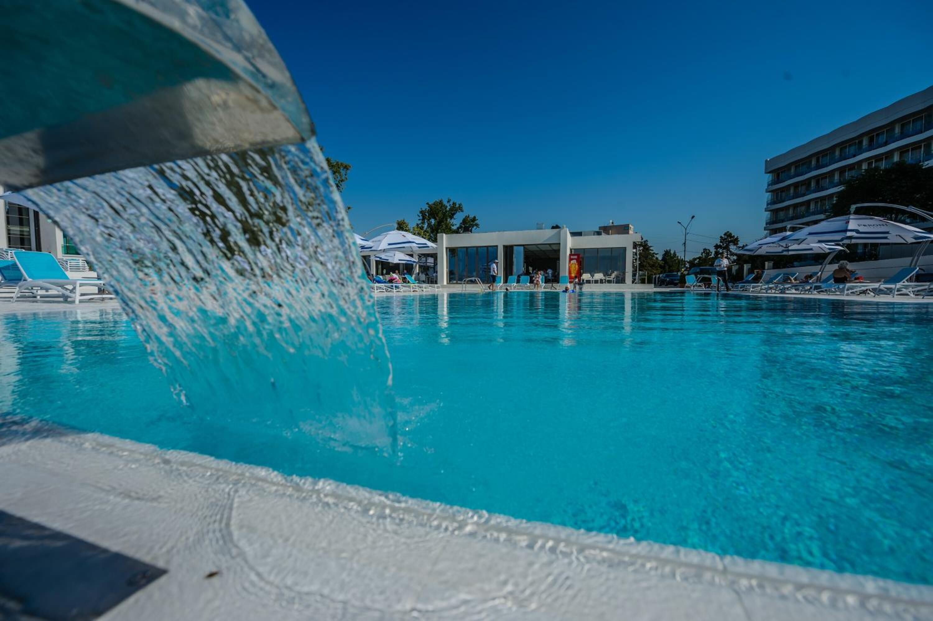 Una piscina con agua azul cristalina, sillas de descanso y un edificio al fondo.