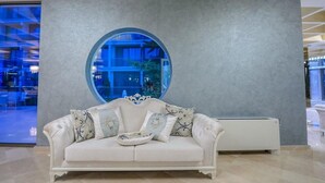 Un sofá de cuero blanco con cojines florales en un vestíbulo moderno con un amplio ventanal circular y un radiador blanco.