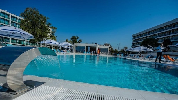 Una piscina con sillas de descanso y sombrillas, rodeada de edificios modernos.