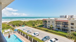 Un hotel con piscina, vistas a la playa y un estacionamiento con varios coches.