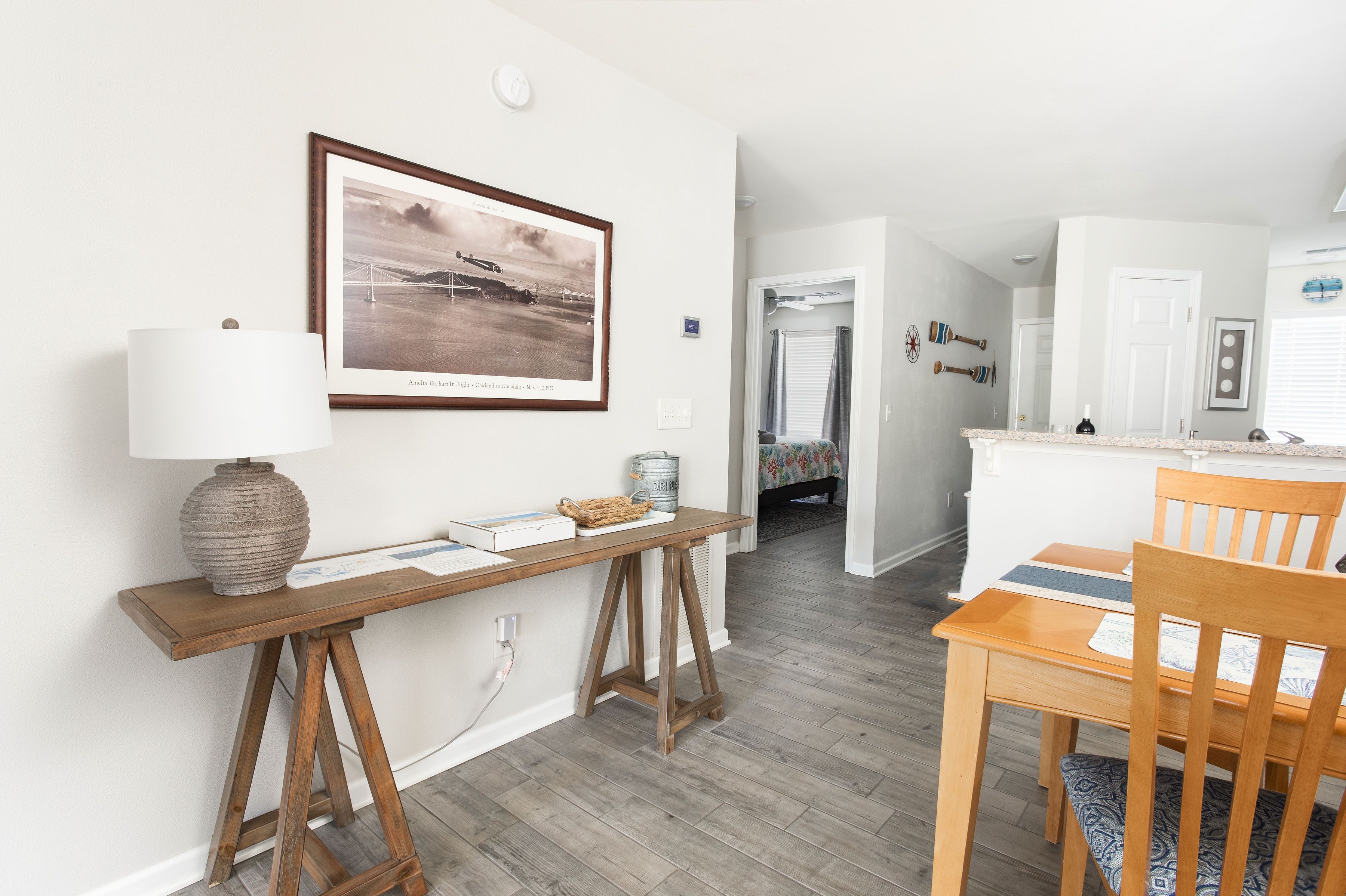A modern interior with a wooden desk, a framed photograph, and a dining area with a wooden table and chairs.