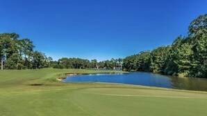 Un parcours de golf avec un étang, entouré d’arbres et offrant une vue sur un ciel dégagé.