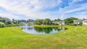 Un terrain de golf bien entretenu, agrémenté d’un étang, et entouré d’une végétation luxuriante et de bâtiments résidentiels.