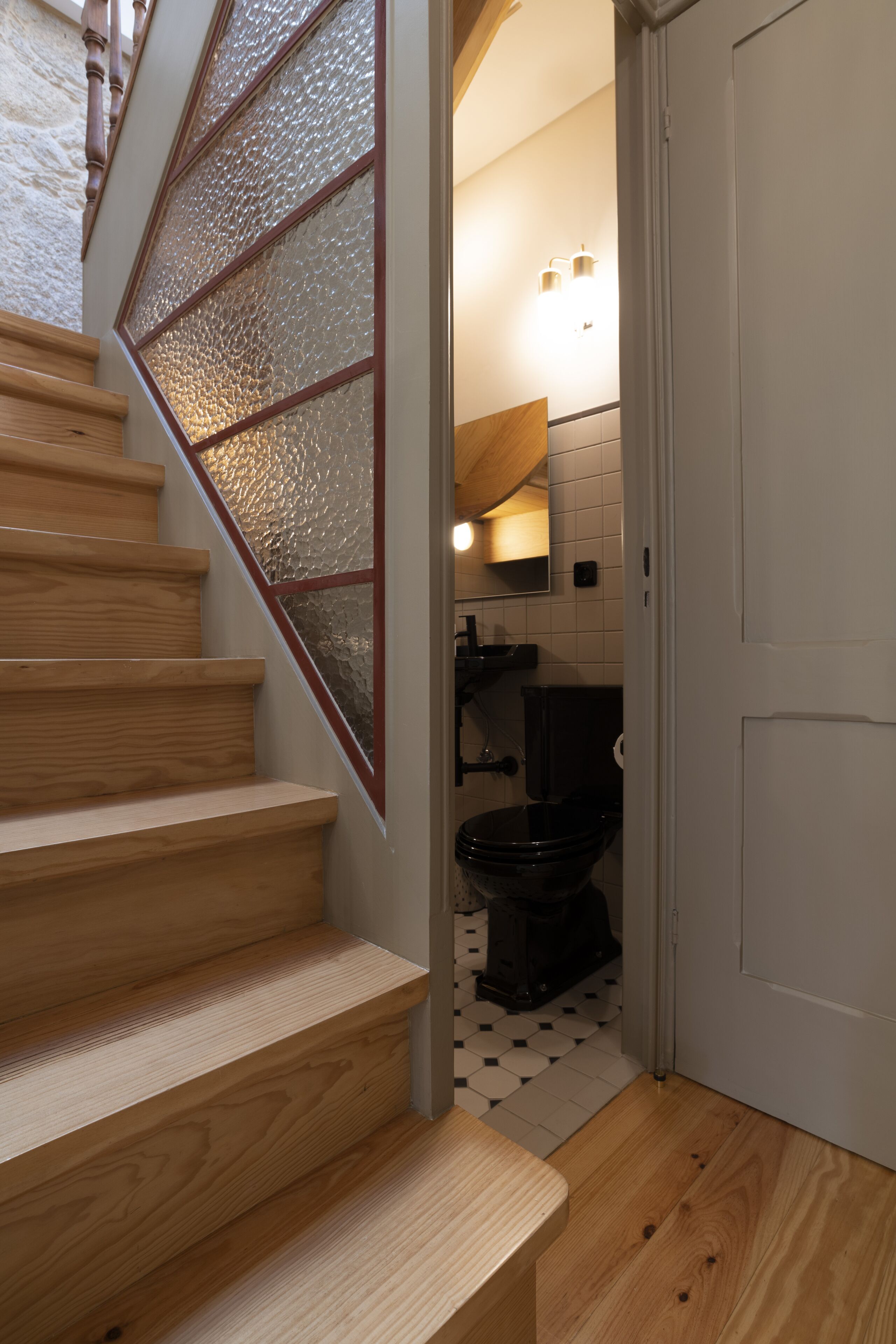 A wooden staircase with a textured glass panel on the right, leading to a bathroom with a toilet and a sink.