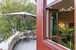Un espace de restauration extérieur moderne, avec une table et des chaises, un grand parasol et une vue sur une zone boisée.