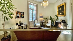 A room with a large window, a chandelier, a painting, and a potted plant.