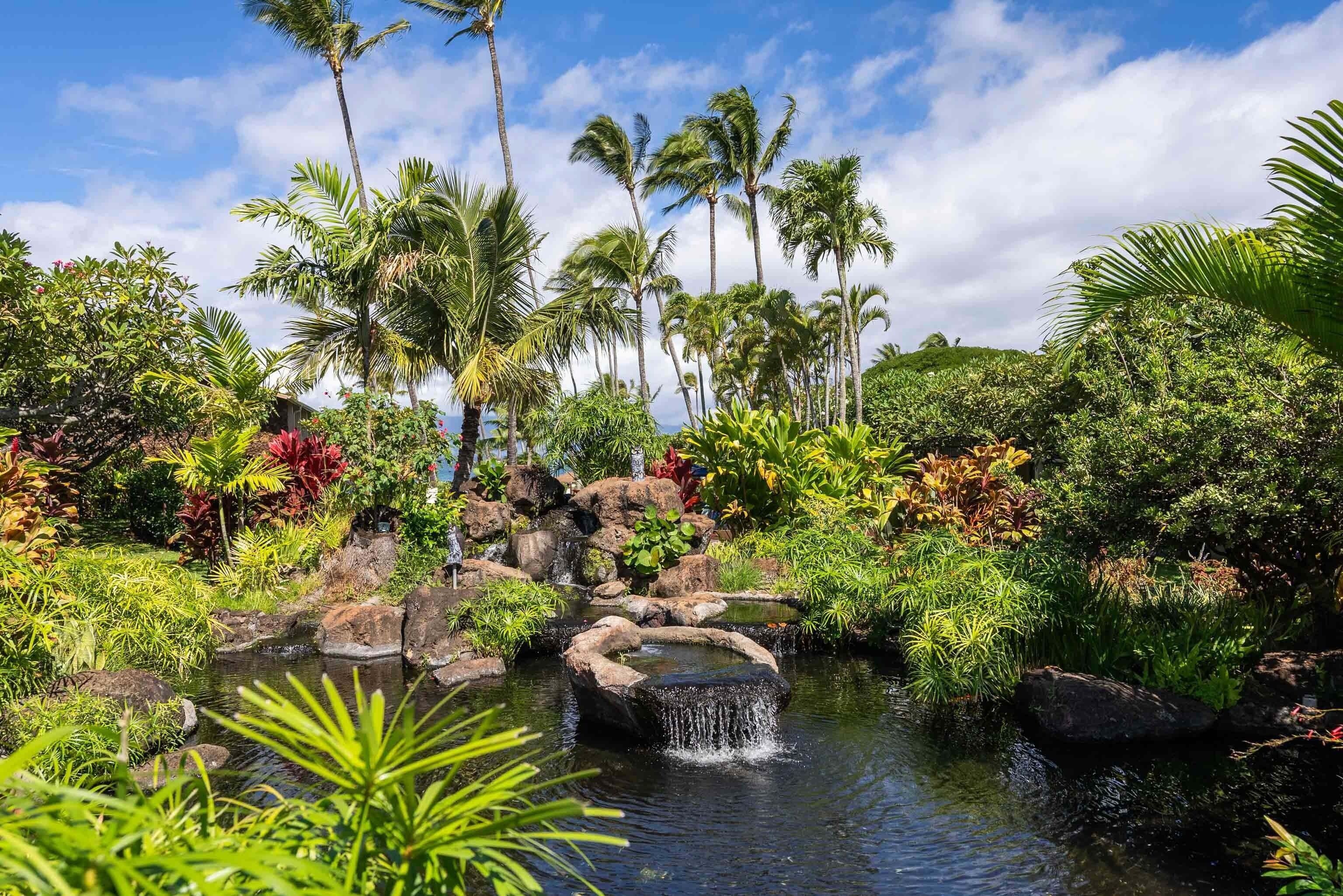 Un jardín tropical con una cascada pequeña, palmeras y diversas plantas.