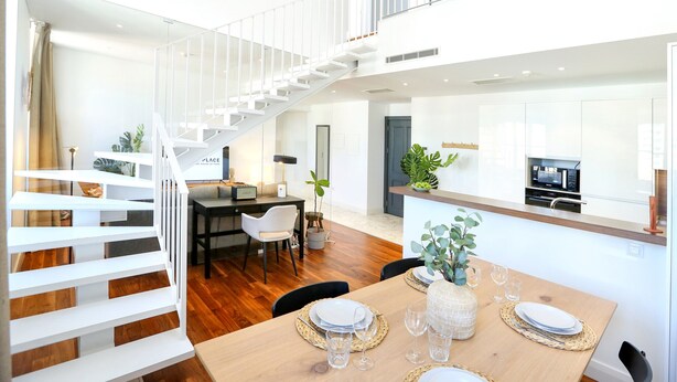 A spacious living area with a wooden dining table set for four, a white staircase, and a kitchen area with modern appliances. - Zen and Tan Apartment (Faro)