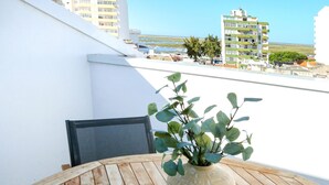 A wooden table with a book and a vase of green plants on a balcony overlooking a cityscape. - Zen and Tan Apartment (Faro)