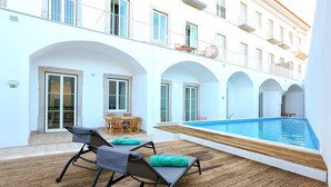 A poolside area with lounge chairs and a table, surrounded by white buildings with arched doorways. - Zen and Tan Apartment (Faro)