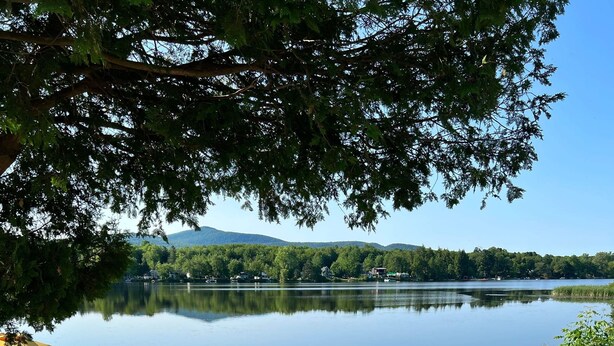 A wooden deck with a pathway leading to a lake, surrounded by greenery and a white fence. - Cottage Tranquility family waterfront mountains (Dunham)