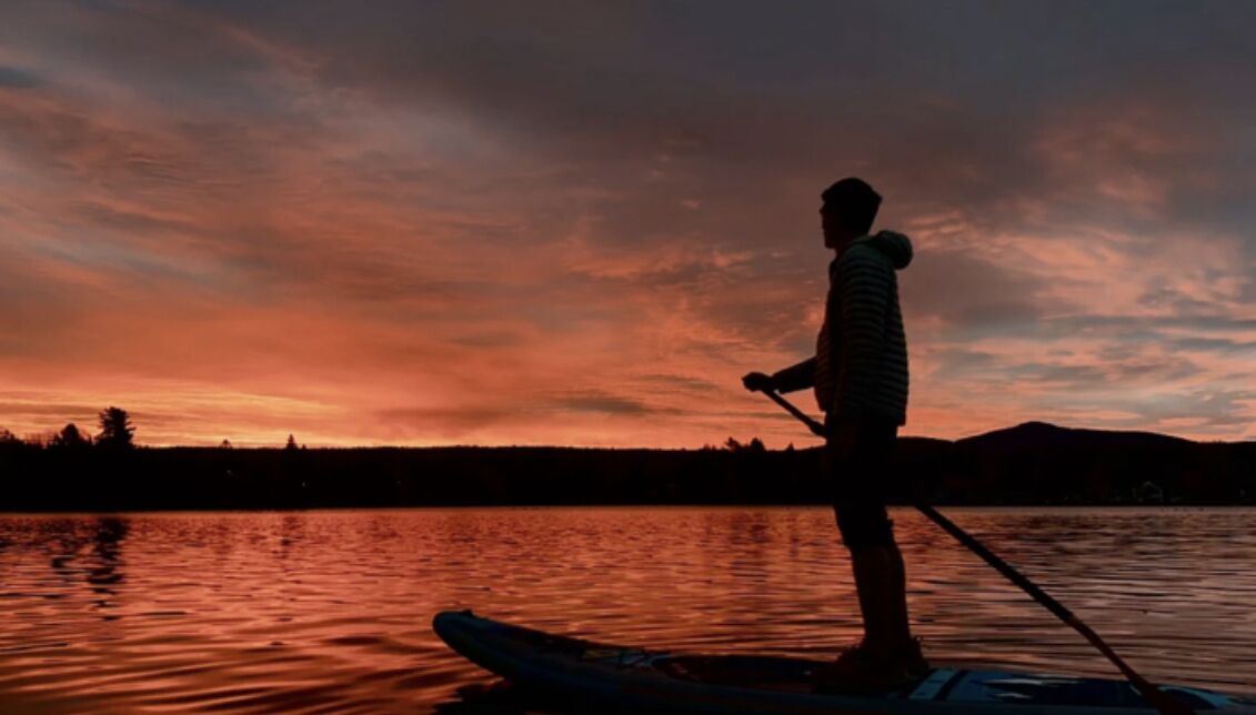 Une personne pratiquant le paddle sur une étendue d'eau calme au coucher du soleil.
